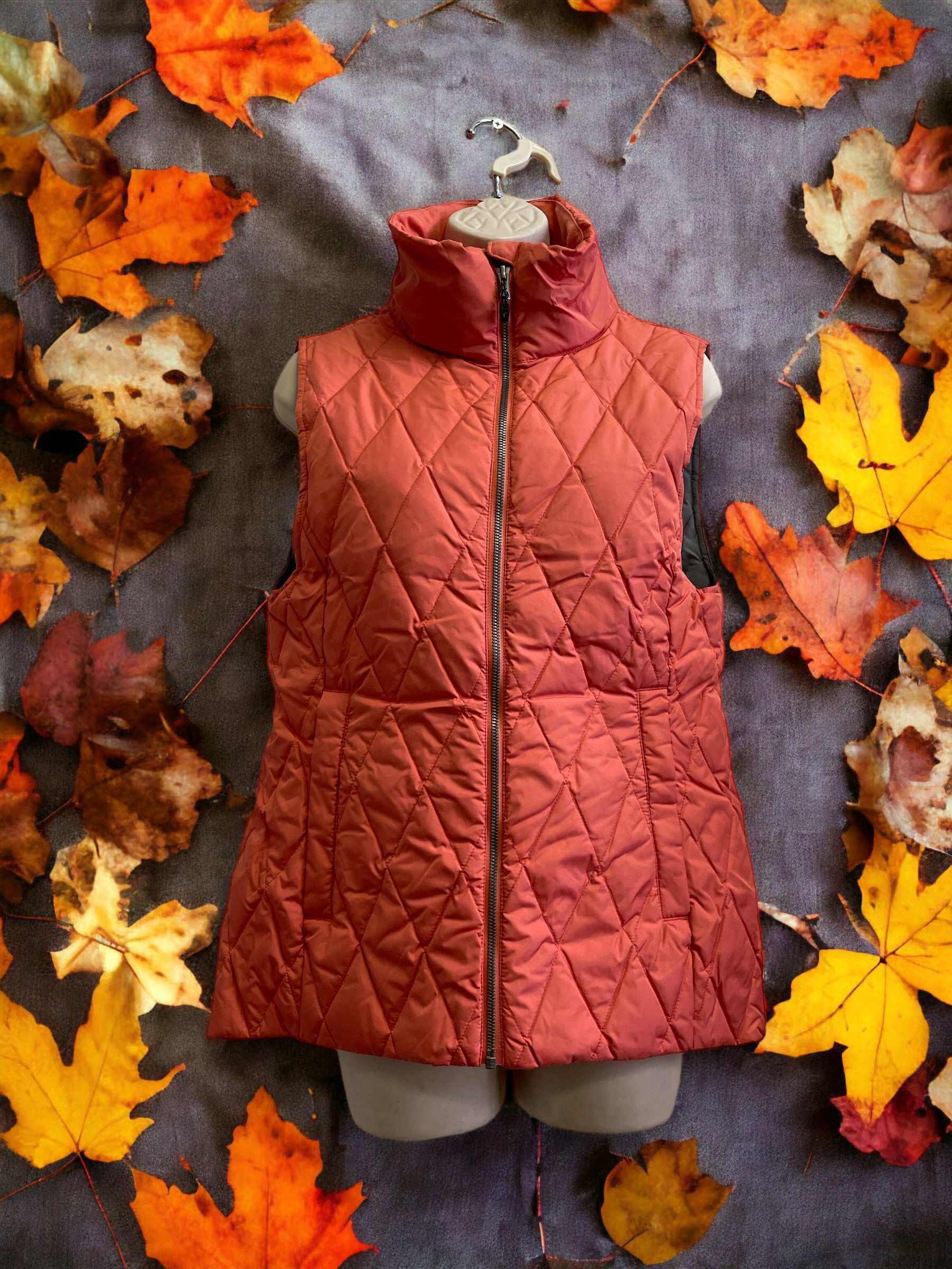 Burnt orange down vest with quilted design, surrounded by fall leaves.