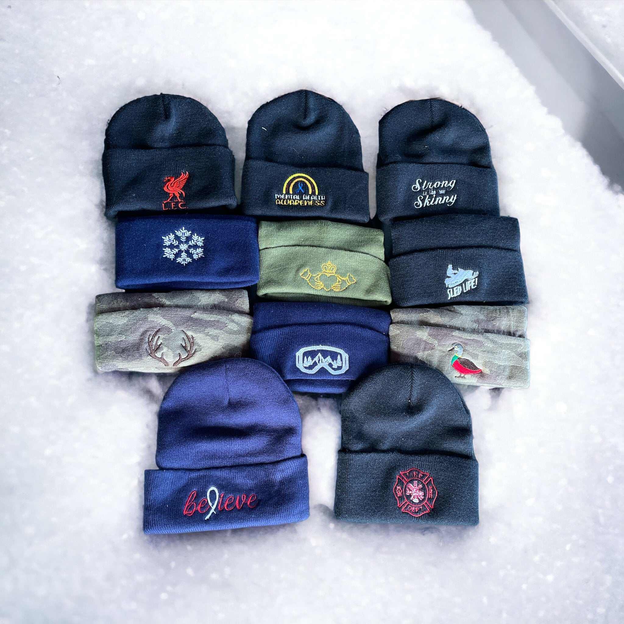 Collection of warm knit hats with various embroidered logos in different colors laid out on snow background