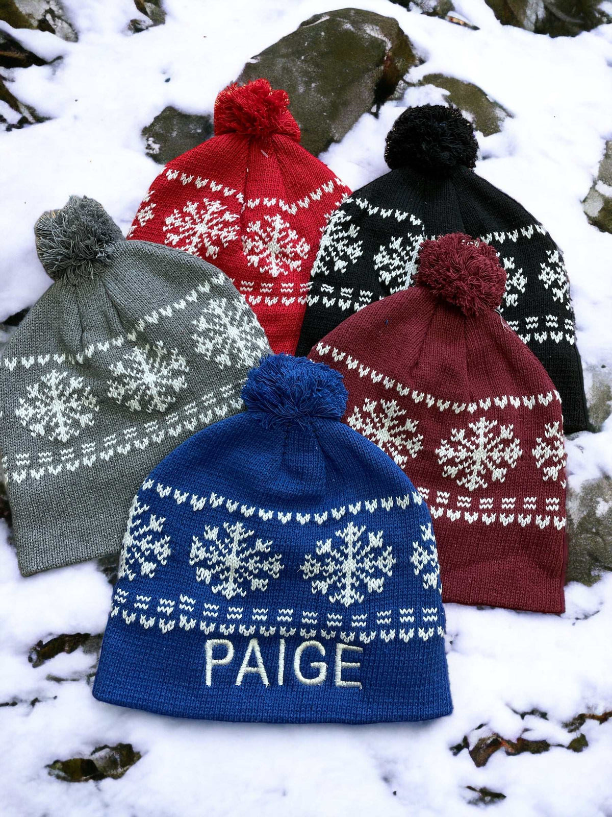 Snowflake knit hat with personalized name in various colors on snow.