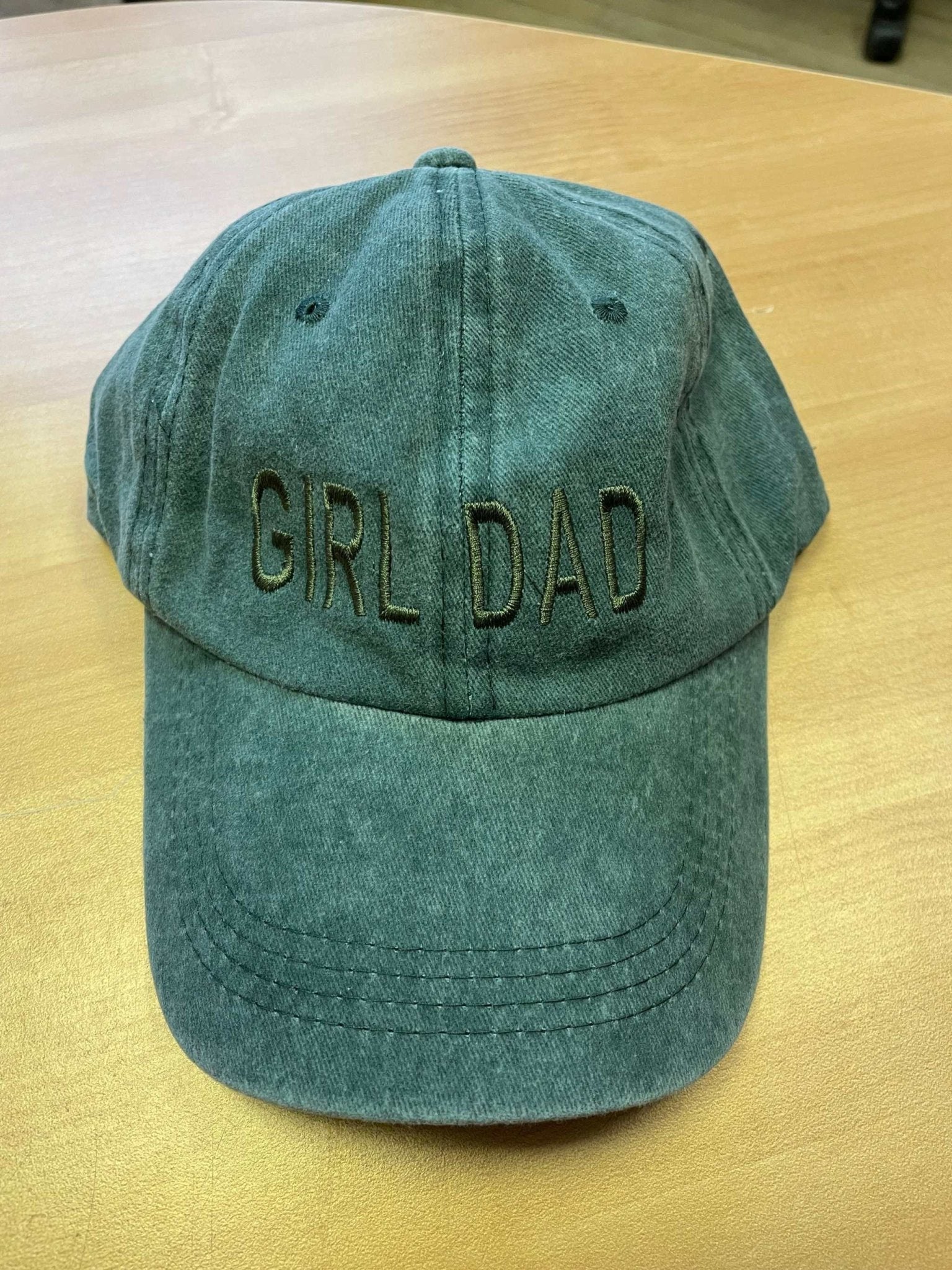 Green "Girl Dad" cotton baseball hat with adjustable strap on wooden surface