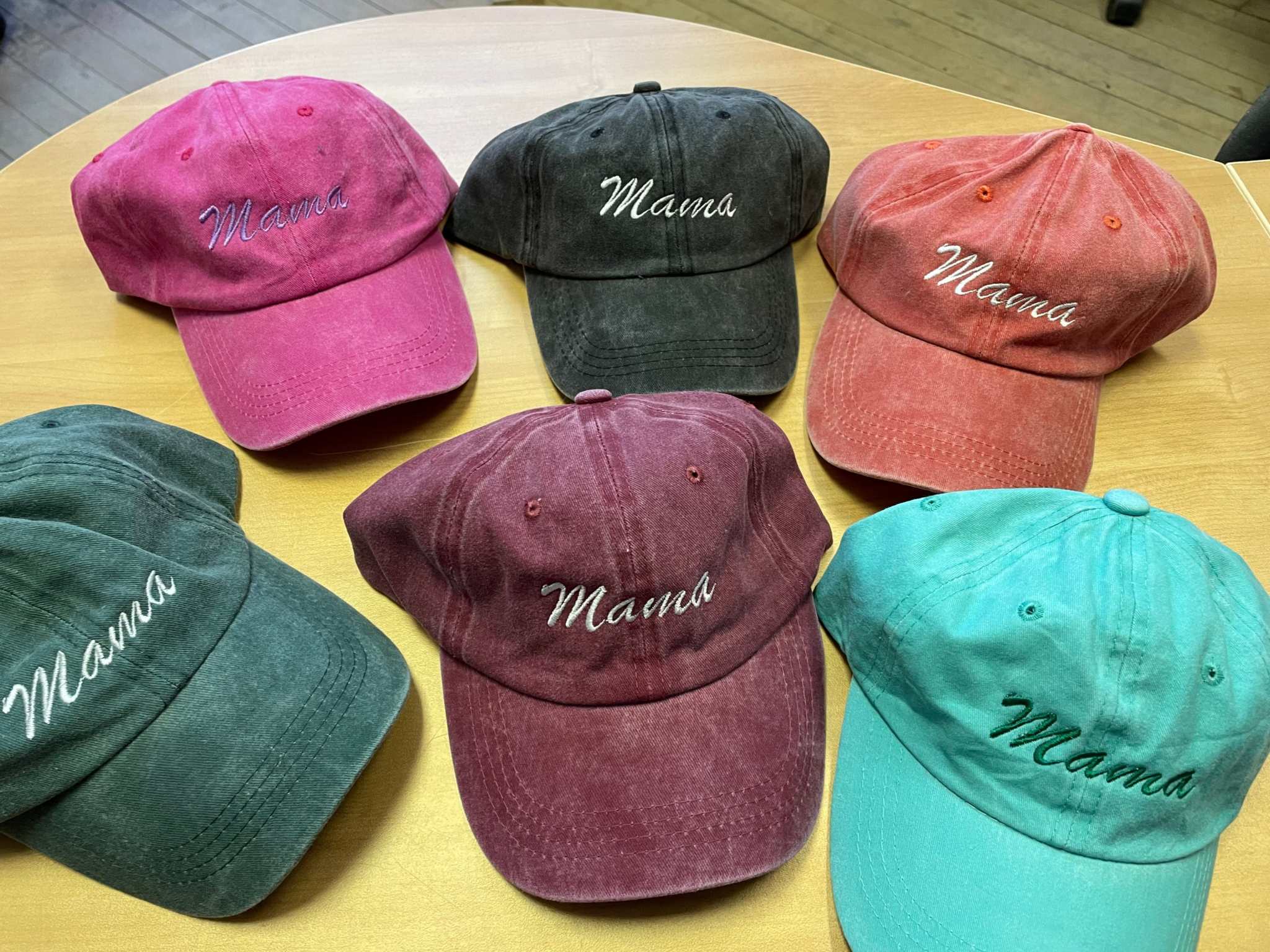 Collection of colorful Mama embroidered cotton baseball hats with adjustable straps on wooden table