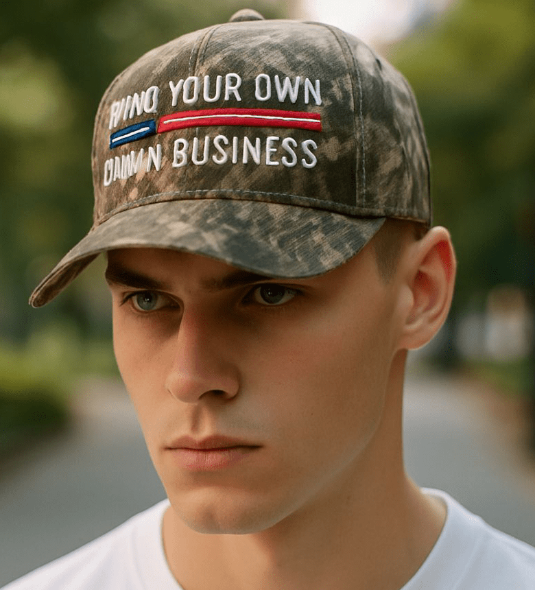 Camo hat with "Mind Your Own Damn Business" embroidered text worn by man outdoors