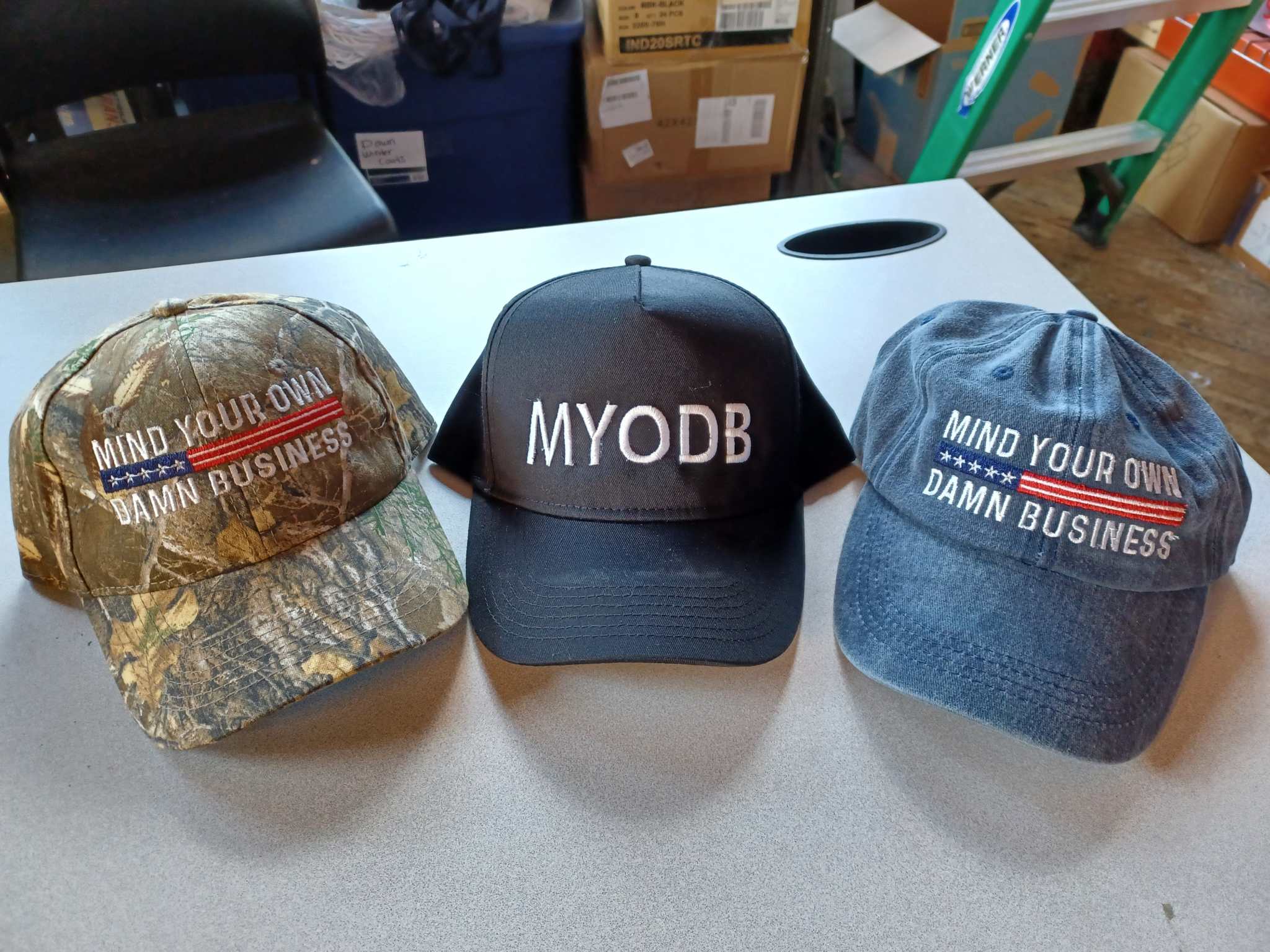 Camo hat with Mind Your Own Damn Business embroidery and adjustable strap on table