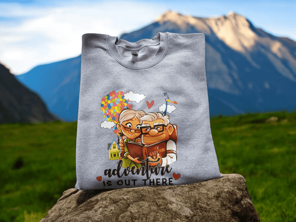 Grey crewneck sweatshirt with Up movie characters and "Adventure is out there" text displayed outdoors on a rock