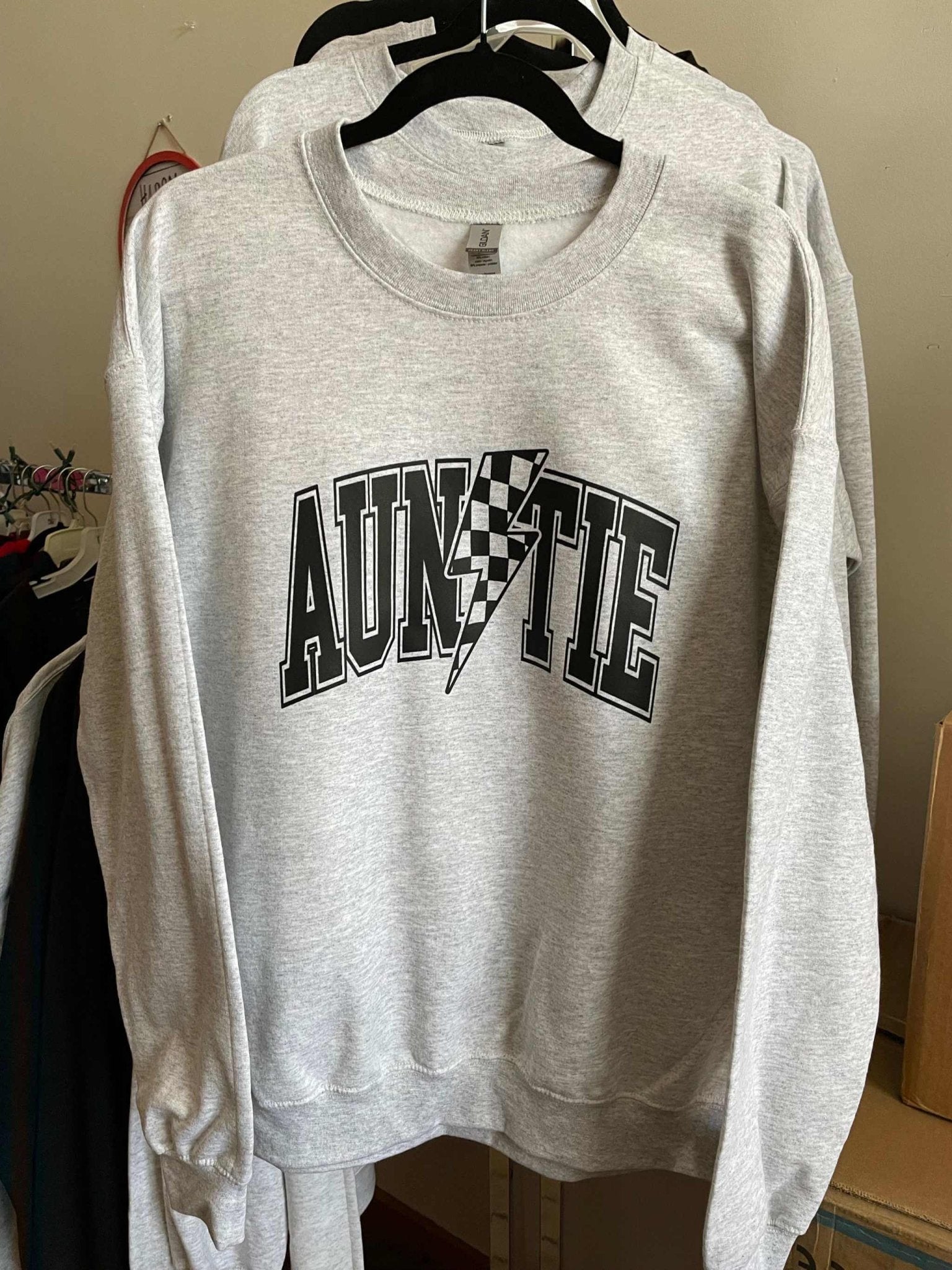 Grey Auntie Racing crewneck sweatshirt with black and white logo design hanging on a rack