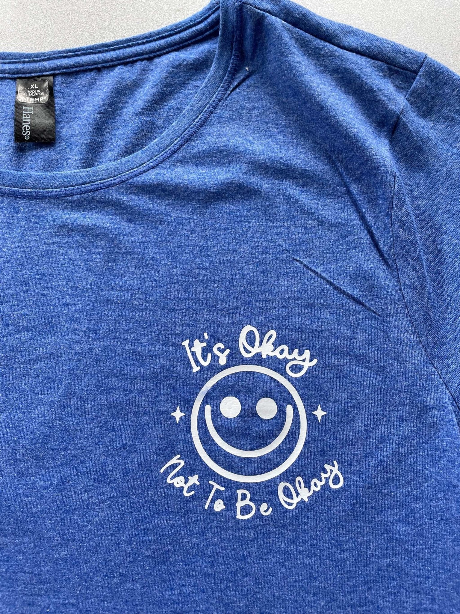 Blue heather women's graphic tee with "It's Okay Not To Be Okay" smiley print