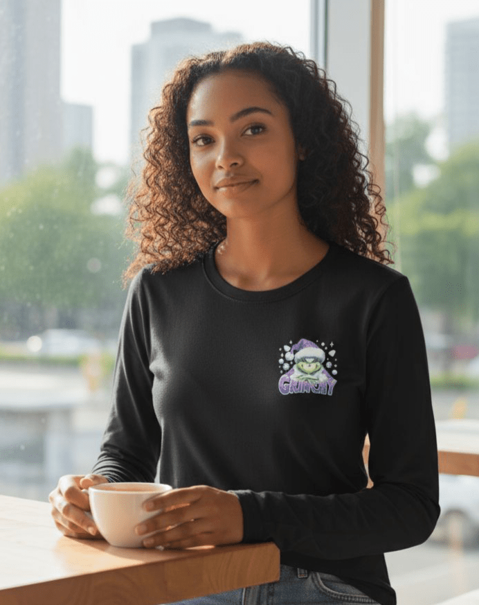 Woman wearing black Grinchy Long Sleeve Teeshirt with Christmas design holding a cup indoors