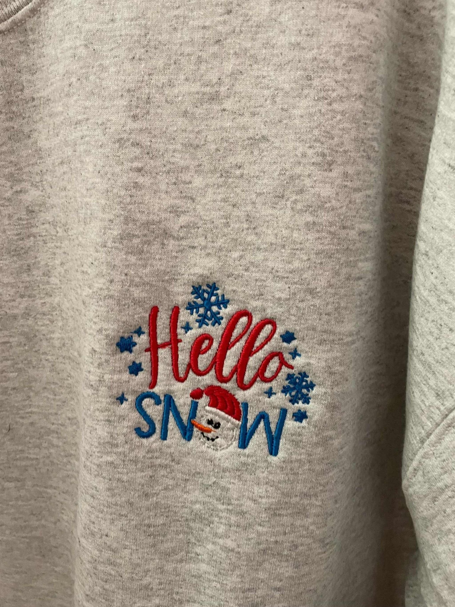 Grey crewneck sweatshirt with "Hello Snowman" embroidered design featuring snowflakes and a snowman face
