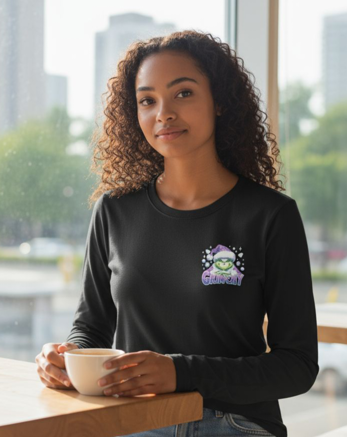 Woman wearing black Grinchy Long Sleeve Teeshirt holding a cup indoors with city view background