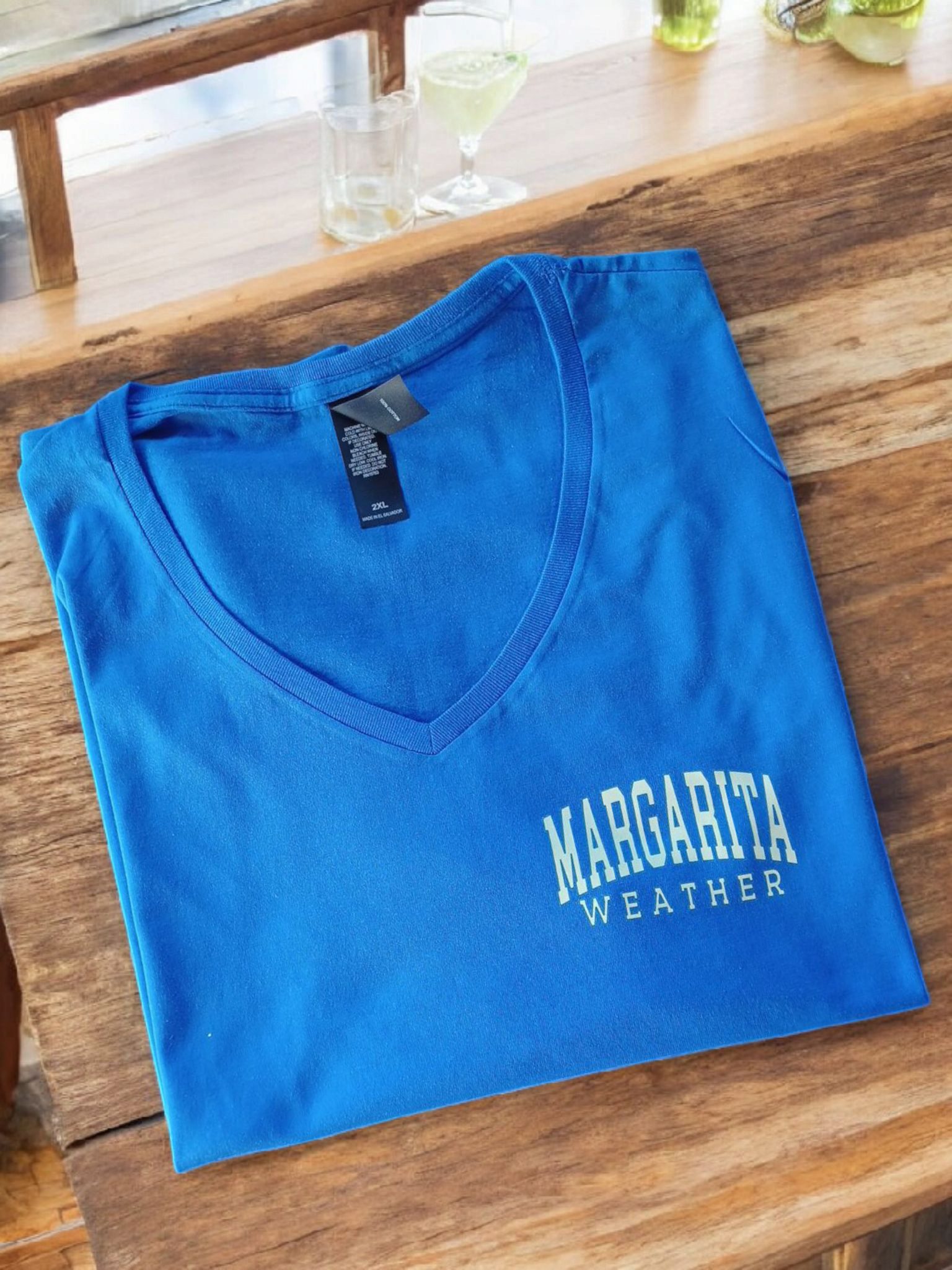 V-neck T Shirt in royal blue with "Margarita Weather" text, folded on a wooden surface.