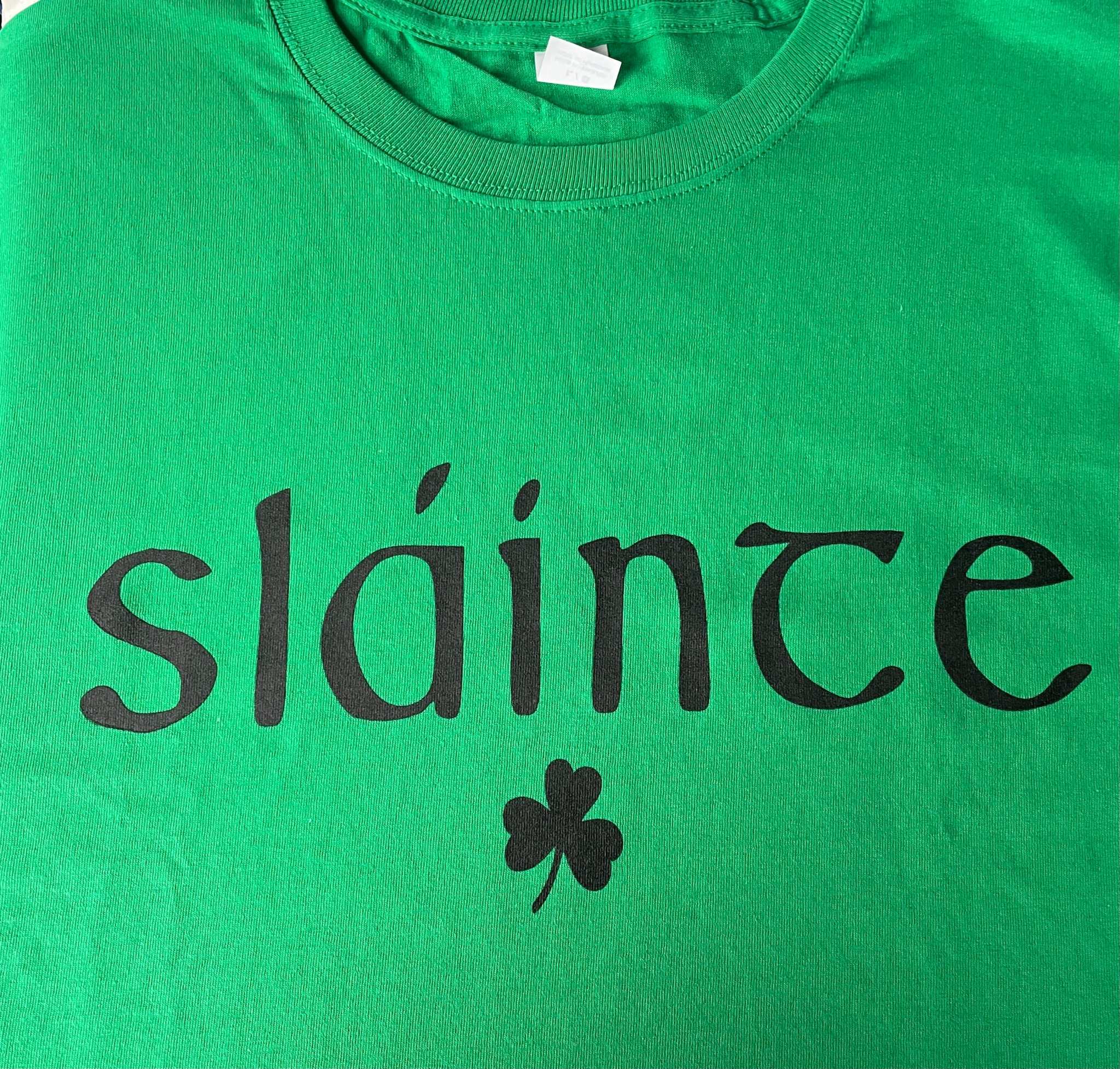 Green cotton t-shirt with black "sláinte" Irish blessing text and shamrock design