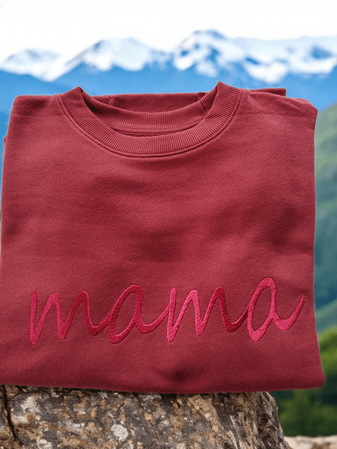 Mama embroidered relaxed fit cotton sweater in deep red color folded outdoors with mountain background