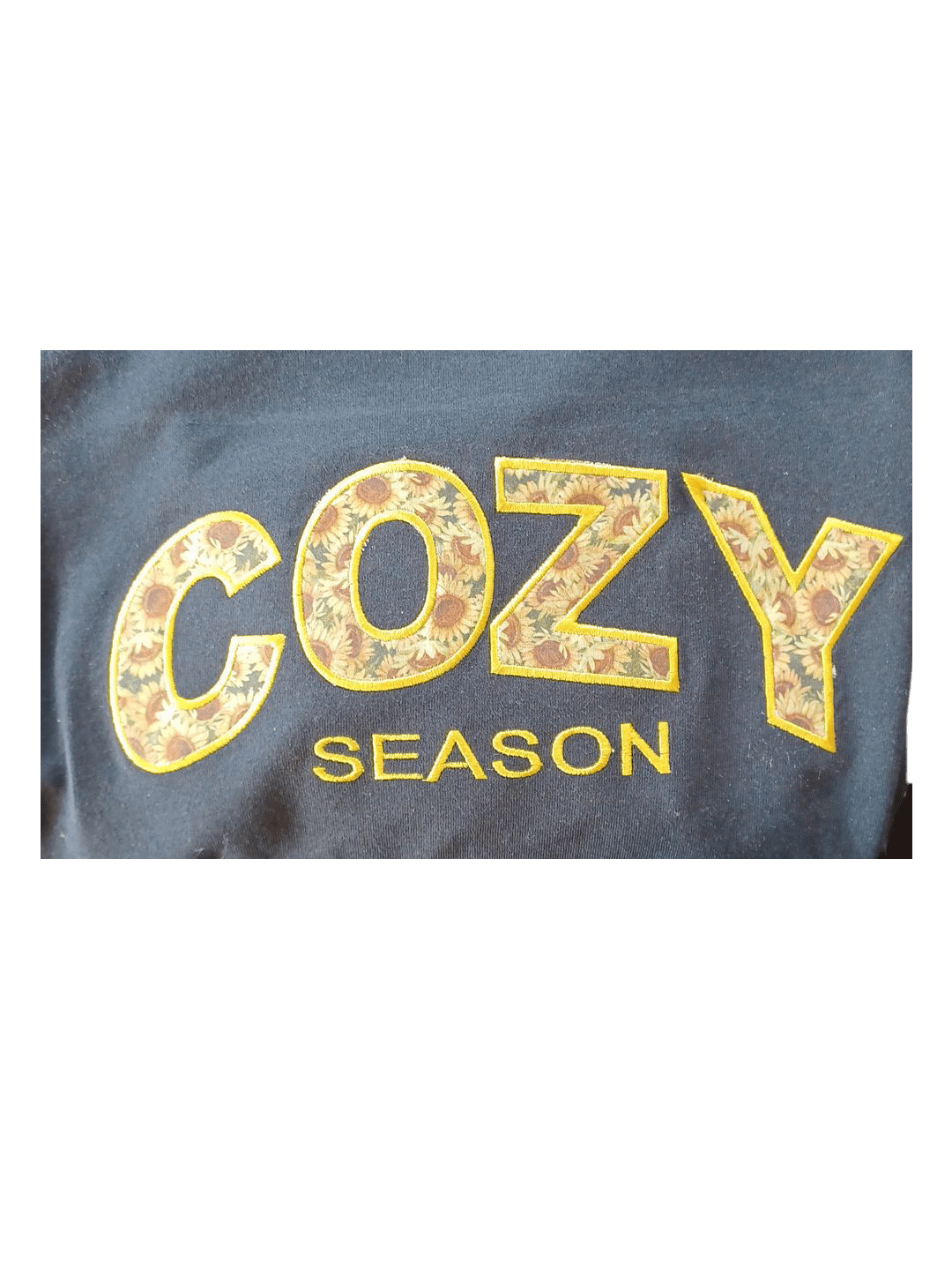 Close-up of Cozy Season embroidered text with sunflower and fall leaf patterns on a black crewneck sweatshirt